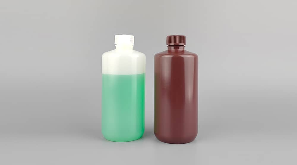 Best Bottles for Developer Solution Storage and Transport 8 A clear HDPE plastic bottle filled with green developer solution sits next to an opaque brown amber bottle, showcasing the contrast between translucent and light-blocking packaging for electronics chemicals. Both have screw-top caps against a gray background.